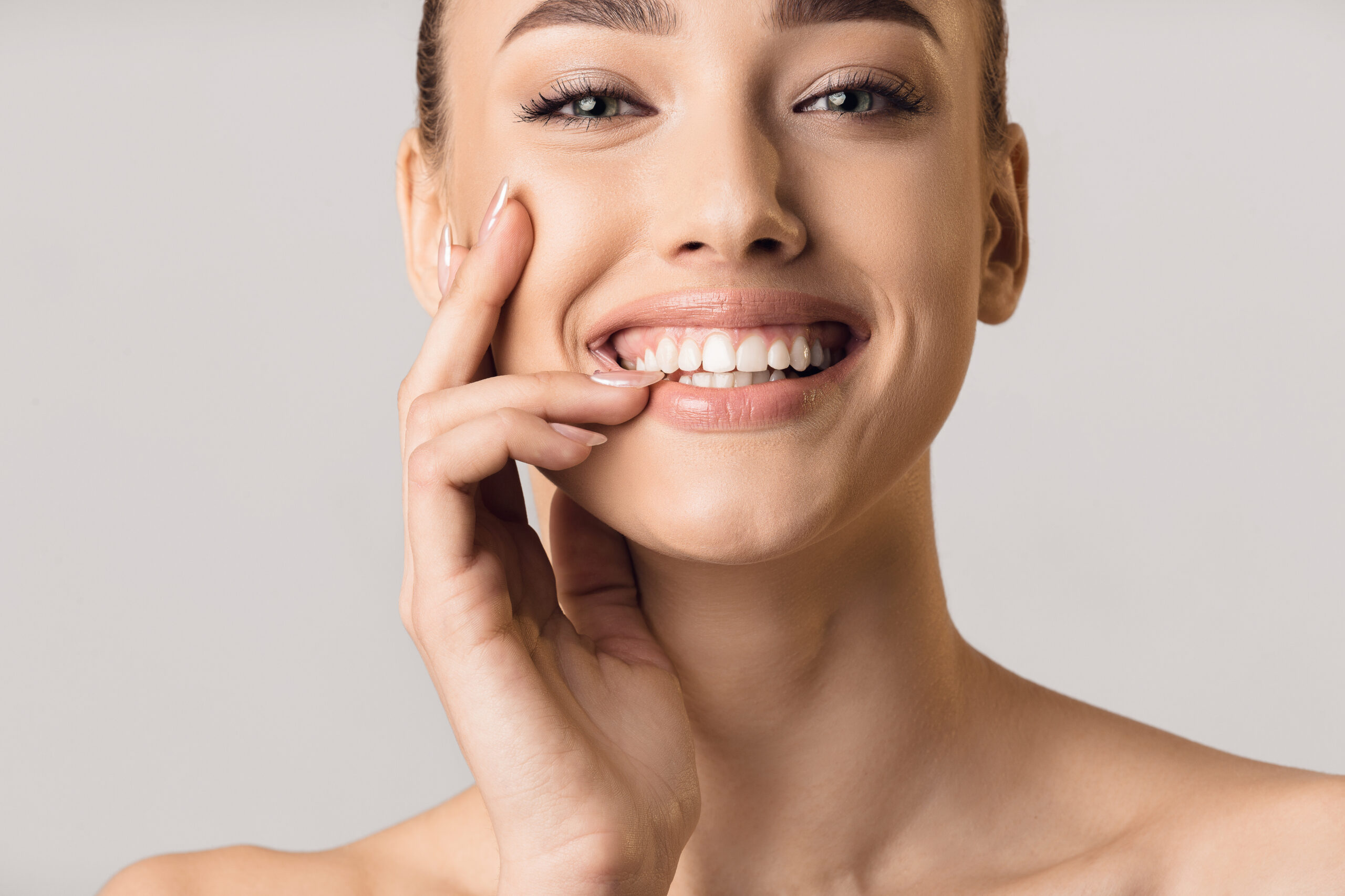 Stomatology concept. Girl with strong white teeth smiling to camera, grey background