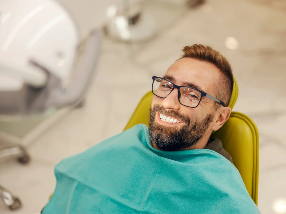Portrait of a patient at dentist office sitting in the chair while smiling at the camera with perfect smile.
