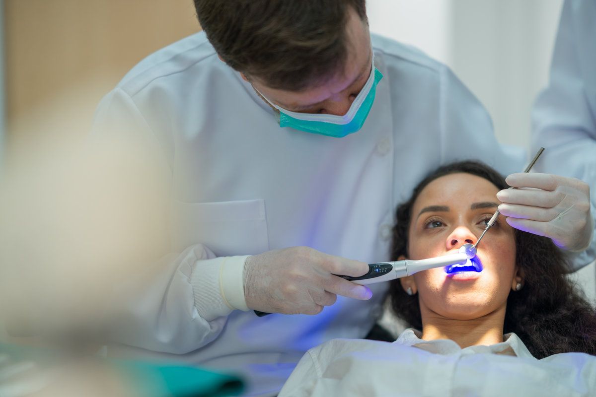 The dentist shines ultraviolet light to make the fluoride setting and cover patients' teeth in the dental clinic.